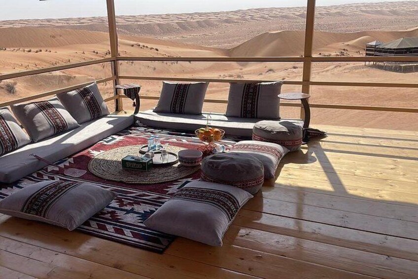 A cozy seating area with cushions and a rug, overlooking a desert landscape with sand dunes. 2