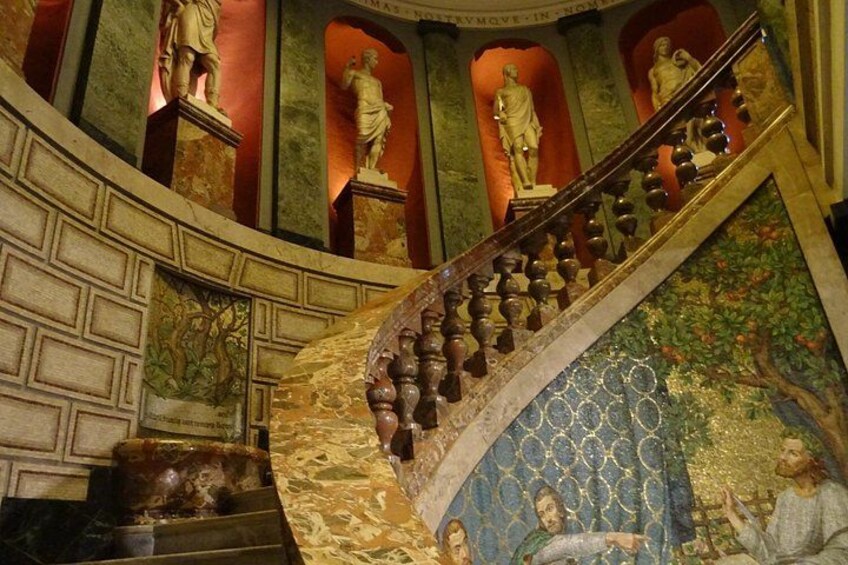 A grand staircase with ornate balustrades, statues, and a mural. 4