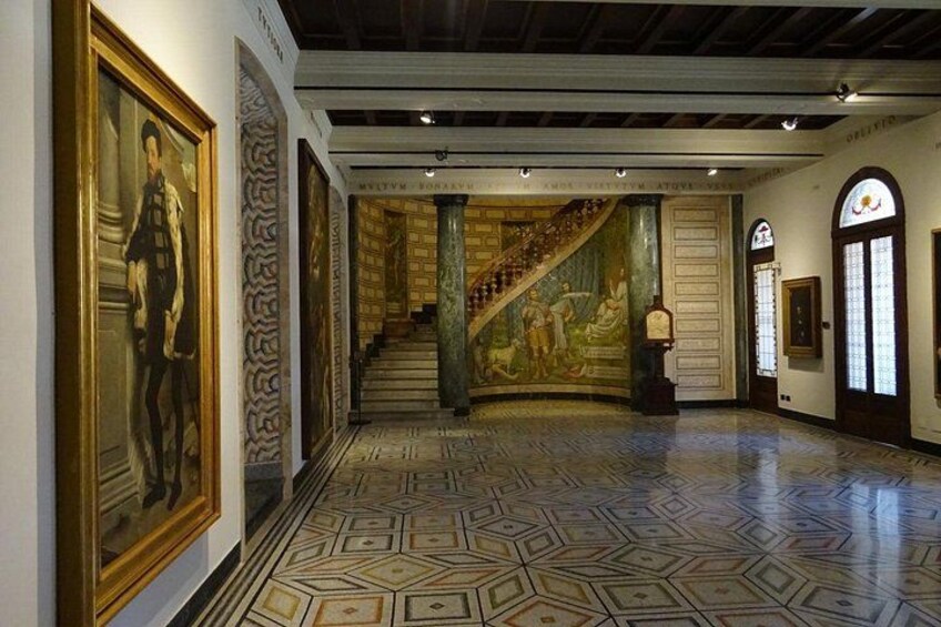 A grand hallway with a patterned floor, a staircase, and a mural. 3
