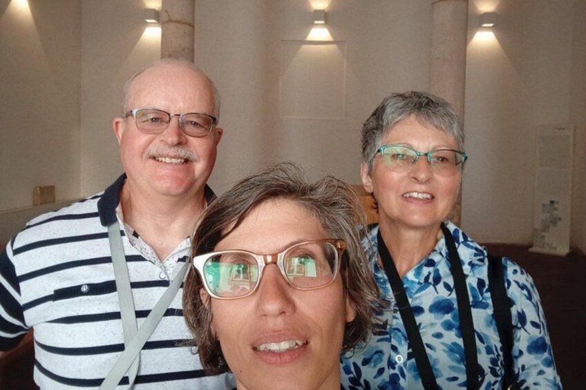 Three people in an indoor setting with columns and wall-mounted lights. 2