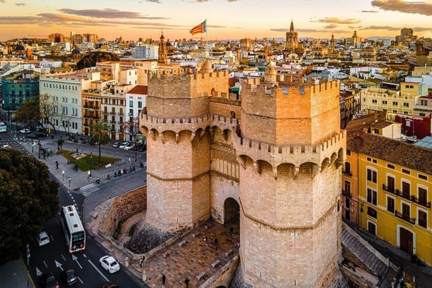A historic tower with two prominent towers, surrounded by a cityscape with buildings and a clear sky. 2