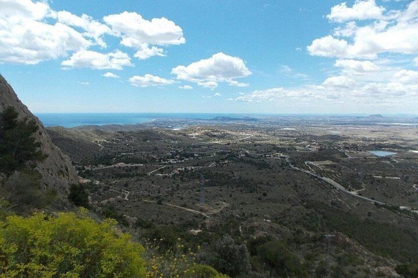 A mountainous landscape with a valley, a winding road, and a distant body of water. 2