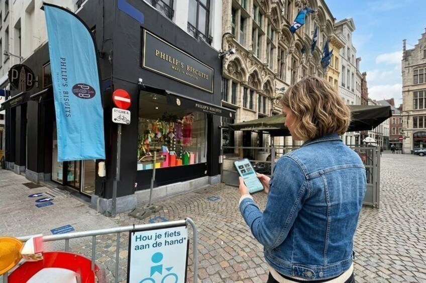A woman using a mobile device in front of a shop named 'Philip's Biscuits.' 4