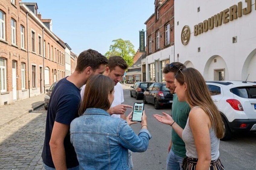 A group of people standing on a cobblestone street, a white car parked on the side, and a building with 'Brouwerij' signage. 2