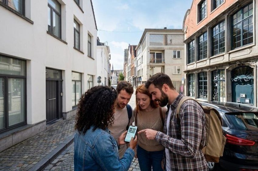 A group of people standing on a cobblestone street, looking at a smartphone. 1