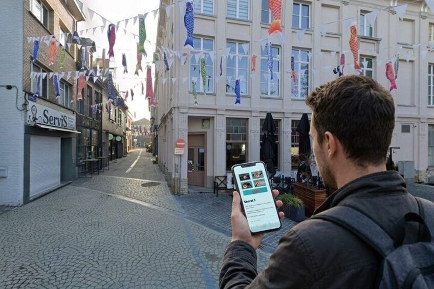 A person using a smartphone on a cobblestone street with buildings and fish-shaped decorations. 3