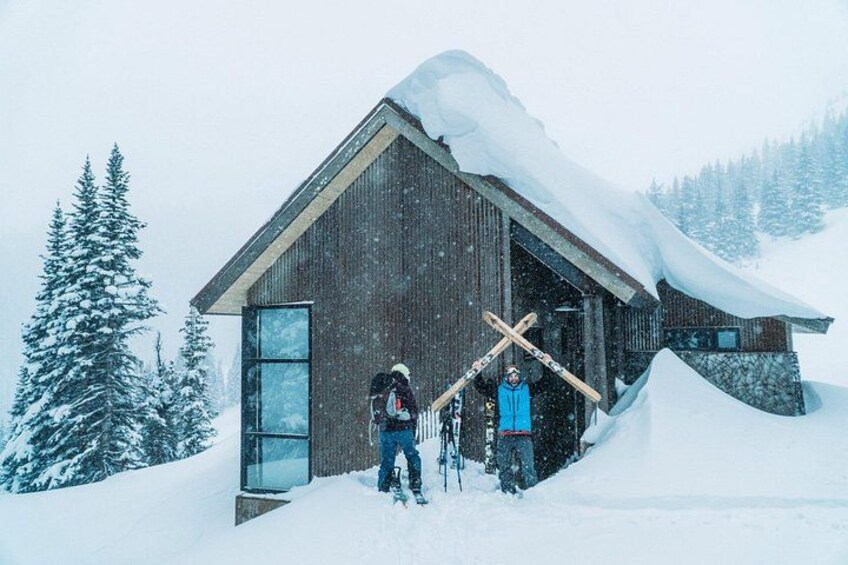 A wooden cabin with a sloped roof covered in snow, surrounded by a snowy landscape and evergreen trees. 2