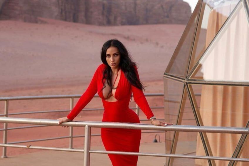 A person in a red dress standing on a balcony with a desert landscape in the background. 4
