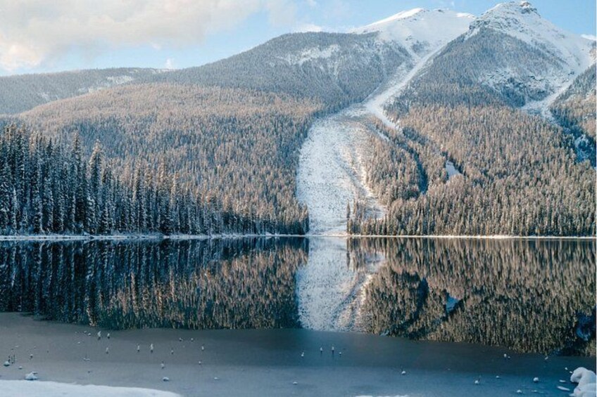 En snötäckt sjö omgiven av tät skog och berg. 3