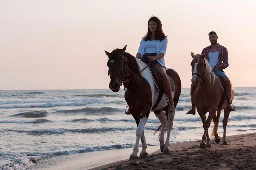Dos personas montando a caballo en una playa con el océano al fondo. 3