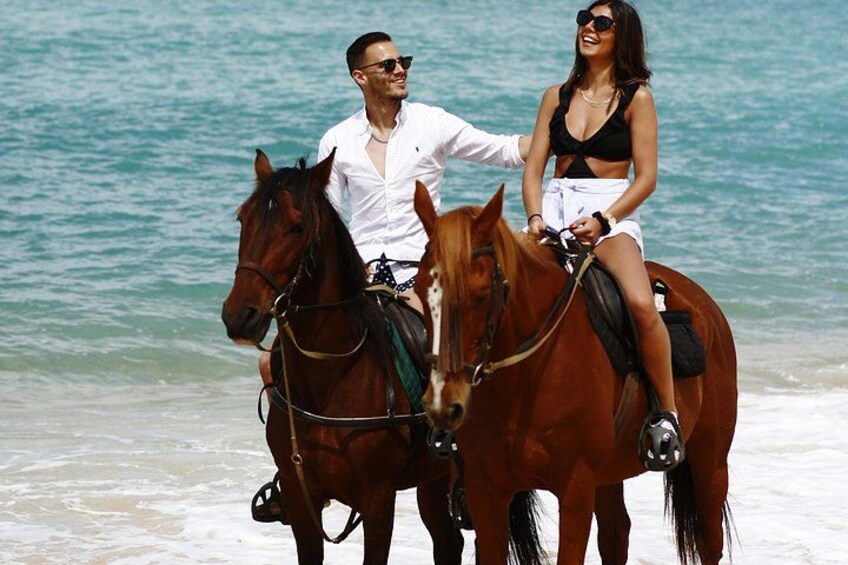 Dos personas montando a caballo en una playa con el océano al fondo. 2