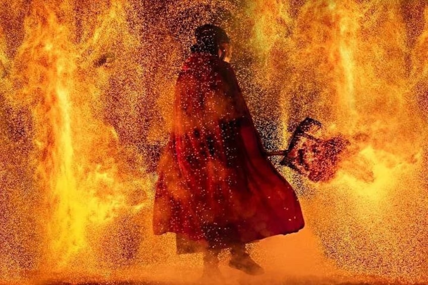 A person in a red cloak standing amidst flames. 1