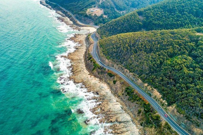 Una carretera costera serpentea a través de un paisaje montañoso con abundante vegetación y aguas turquesas cristalinas. 2
