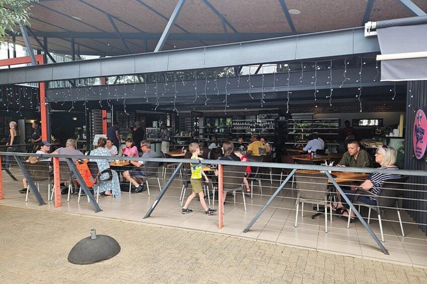 An outdoor seating area with tables and chairs, a covered walkway, and a storefront in the background. 4