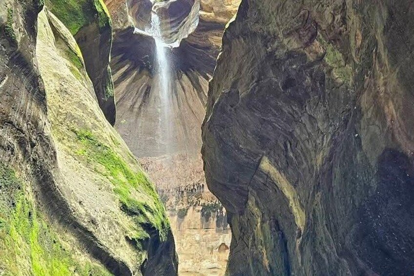 A canyon with a waterfall, rocky cliffs, and a narrow passageway. 5