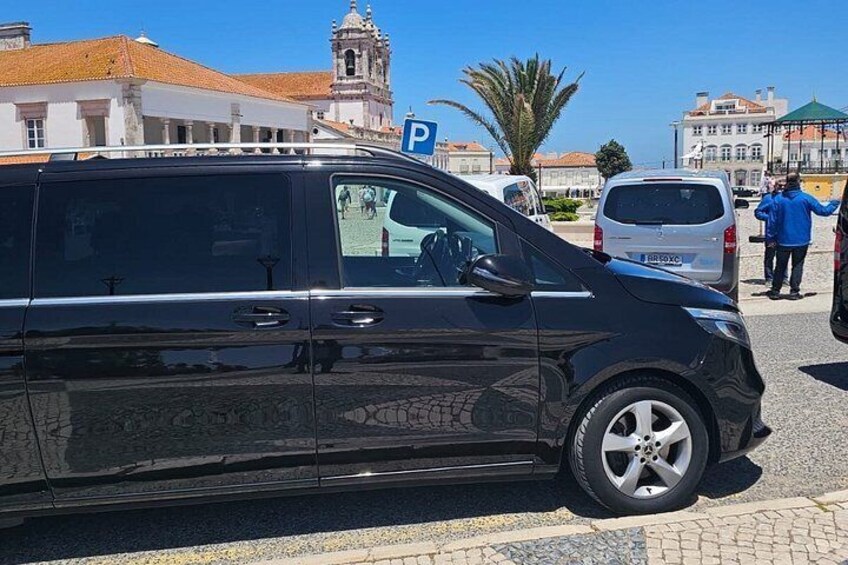 Una furgoneta negra estacionada en una calle con un letrero azul de estacionamiento en la parte superior, una furgoneta blanca al fondo y un edificio con una torre del reloj. 2