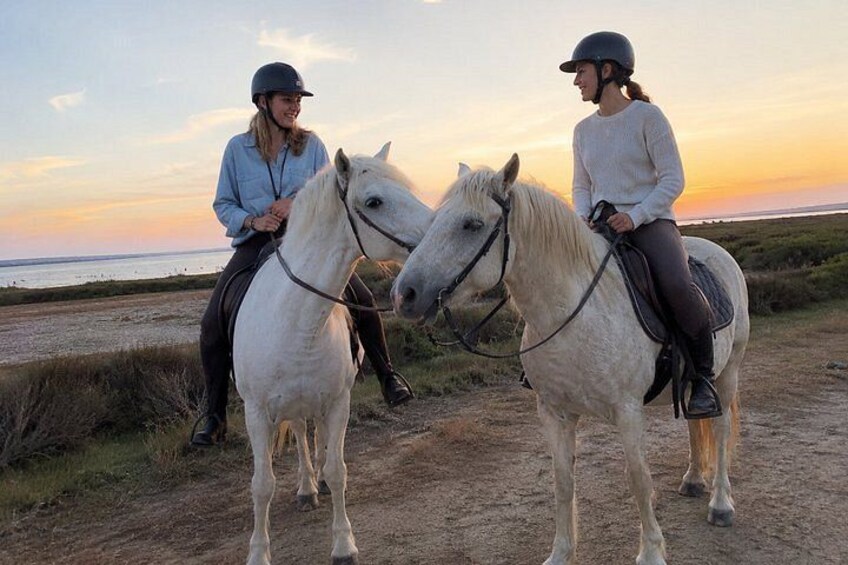 Two people riding white horses on a dirt path with a sunset in the background. 5