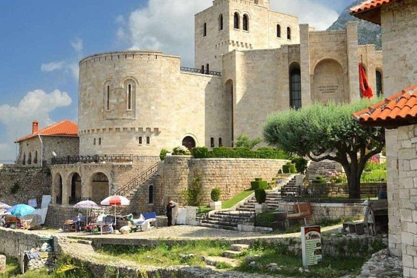 A historic stone building with arched windows and a tower, surrounded by a well-maintained garden and a small staircase leading up to it. 4