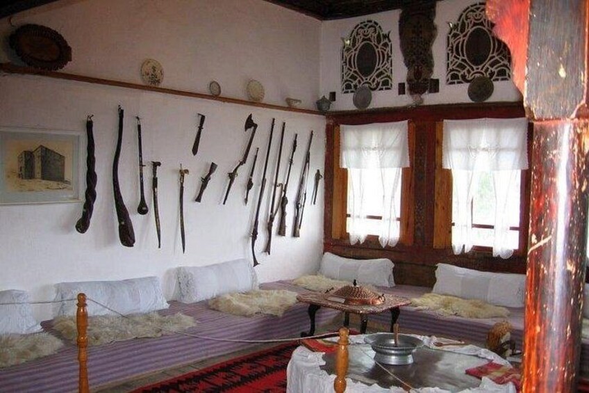 A room with a collection of antique weapons on the wall, a bed with white bedding, and a large window with curtains. 2