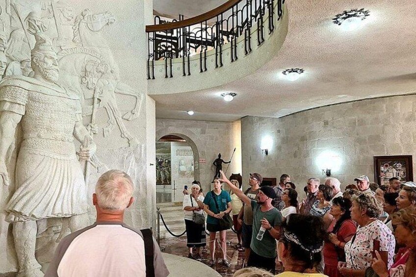 A crowd of people gathered around a statue in a building with a staircase and a railing. 5