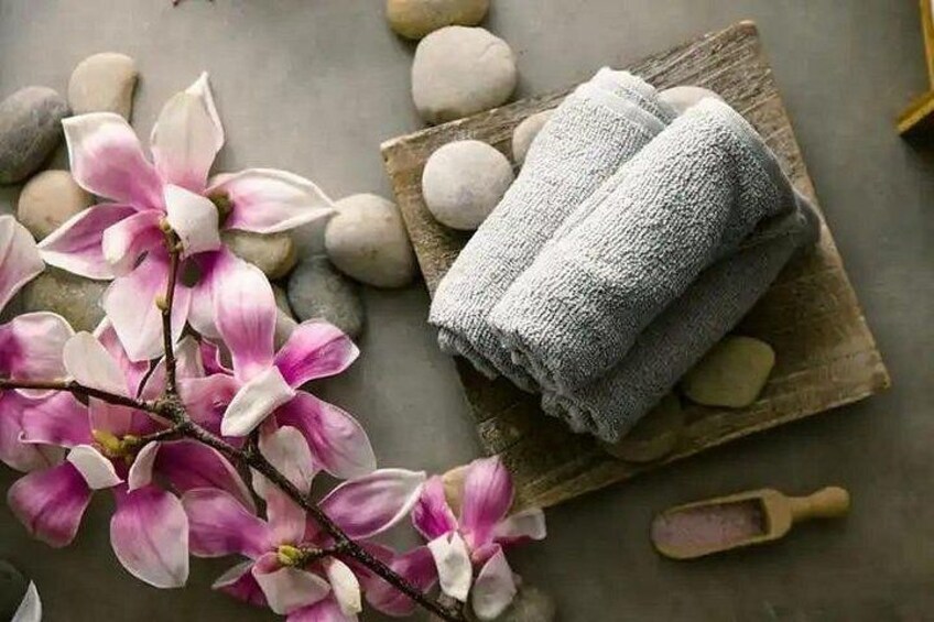 A wooden board with folded towels, a branch of pink flowers, and smooth stones. 3