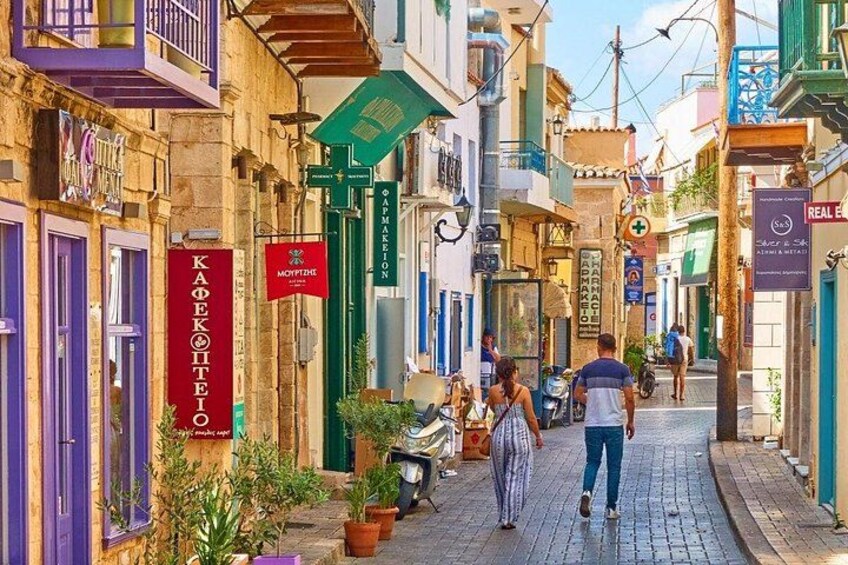 A narrow street lined with colorful buildings, a café, and a pharmacy. 2