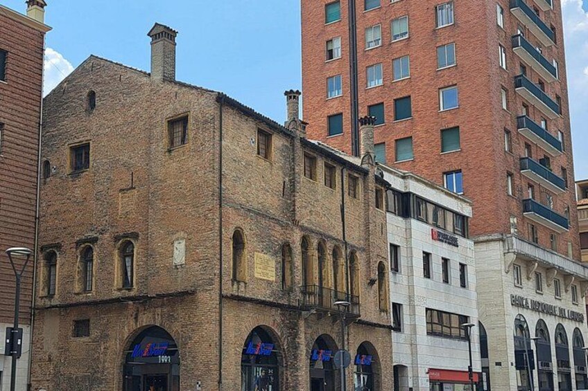 Un edificio histórico con ventanas arqueadas y fachada de ladrillo, junto a un moderno edificio de gran altura. 3