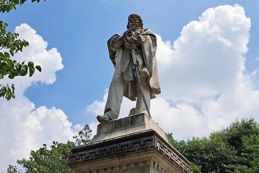 Una estatua de una persona sosteniendo una espada, sobre un pedestal con inscripciones. 5