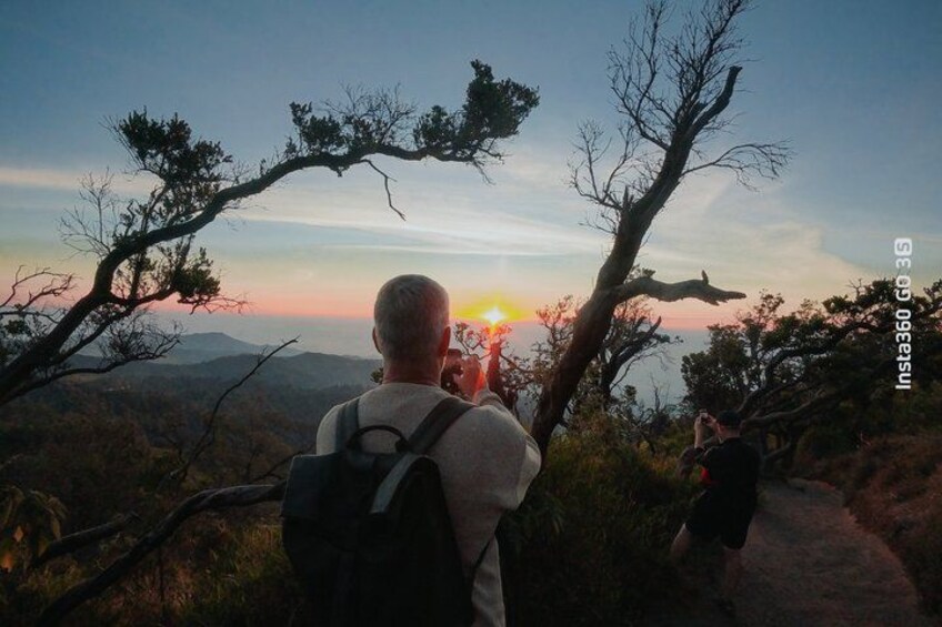 A person taking a photo of a sunset with a mountain landscape in the background. 3