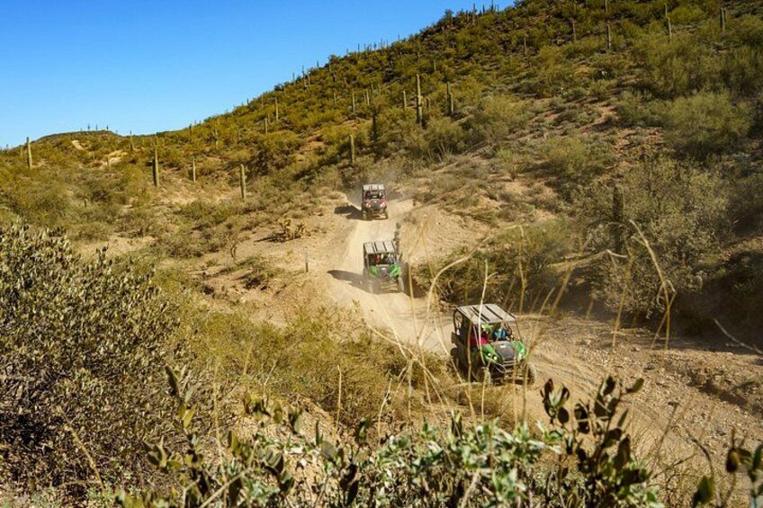 A dirt road with vehicles, surrounded by dry vegetation and hills. 2
