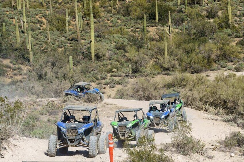 Off-road vehicles on a dirt path in a desert with sparse vegetation. 2