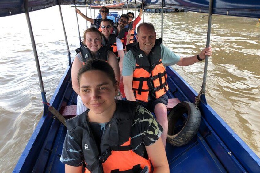A group of people on a boat with life jackets, a tire, and a water body. 2