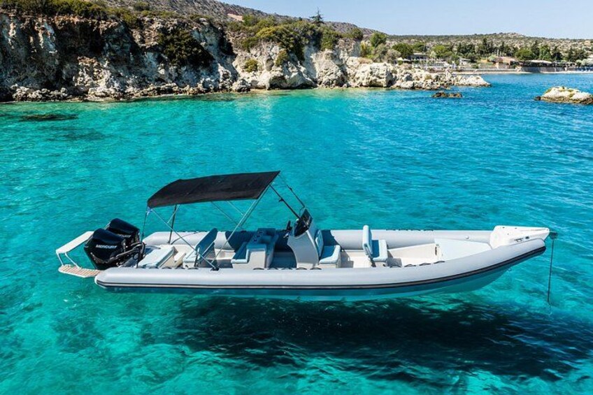 Un bateau pneumatique blanc, surmonté d’un auvent noir, flotte sur une eau turquoise et limpide, avec des falaises rocheuses en arrière-plan. 5