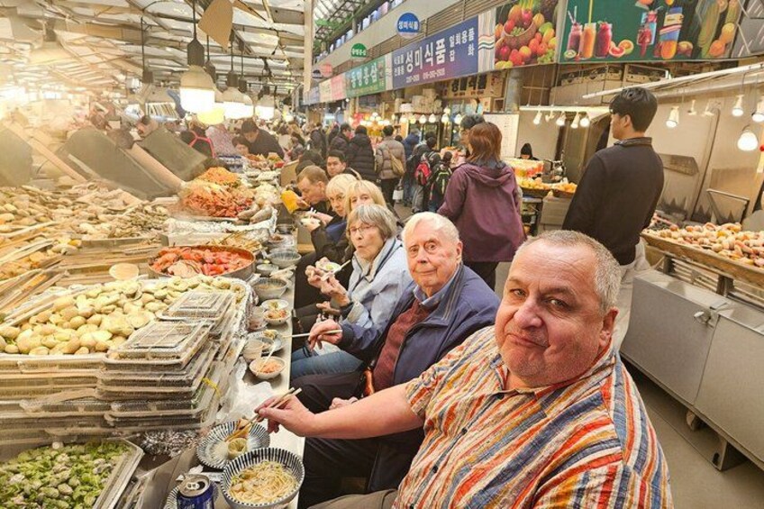 A crowded indoor market with various food stalls and people browsing. 2