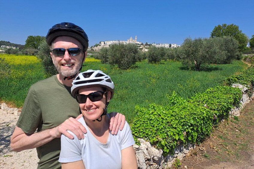 Two people wearing helmets, a green field, and a stone wall. 1