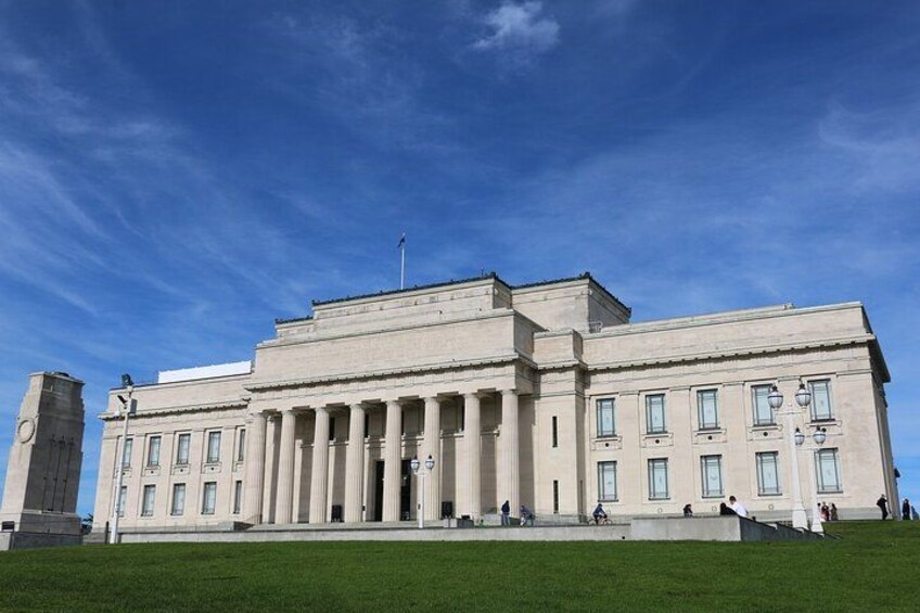 Un grand bâtiment de style classique, doté de colonnes, d’un mât pour drapeau et surplombé d’un ciel bleu clair. 1