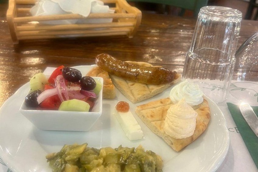 En tallerken med et udvalg af mad, herunder salat, pølse, ost og et wienerbrød. 4