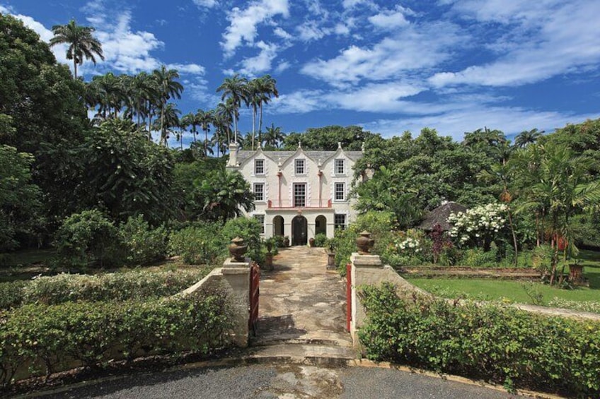 A large colonial-style building with a symmetrical facade, surrounded by lush greenery and palm trees. 2