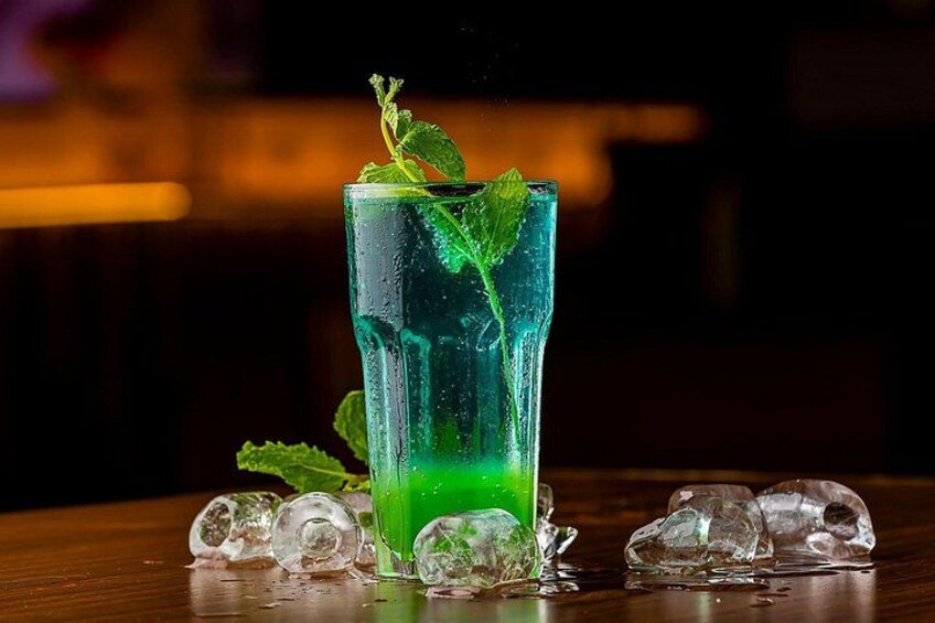 Un vaso alto con una bebida verde, cubitos de hielo y hojas de menta. 2