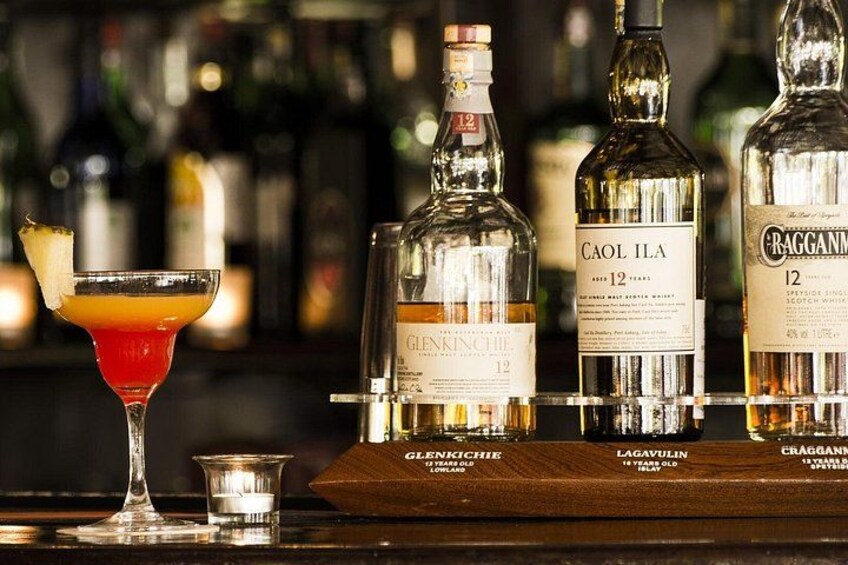 Un bar con botellas de whisky Glenfiddich y Caol Ila, un vaso de cóctel rojo y un vaso pequeño. 5