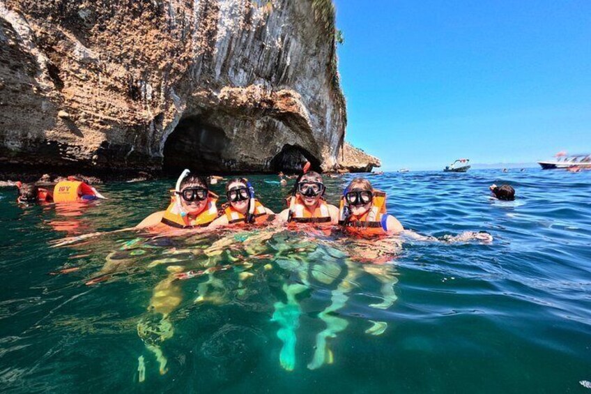 Snorkelers in clear water near a rocky cliff. 5