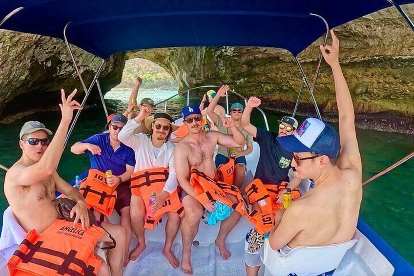 A group of people on a boat, wearing life jackets, with a cave in the background. 2
