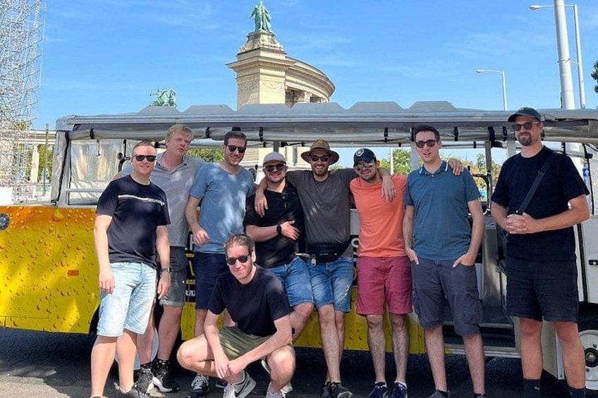 A group of people posing in front of a yellow barrier with a statue in the background. 5