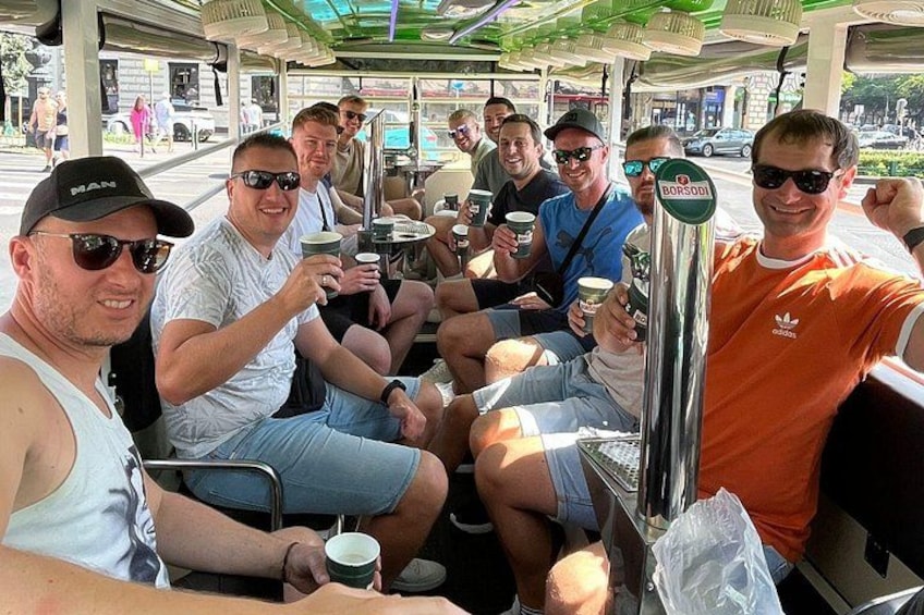 A group of people sitting at tables, holding cups, in an outdoor setting with a green roof. 4