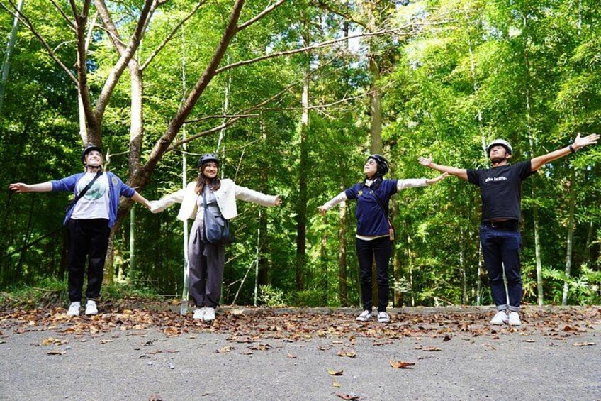 Four people standing on a road with their arms outstretched in a forested area. 2