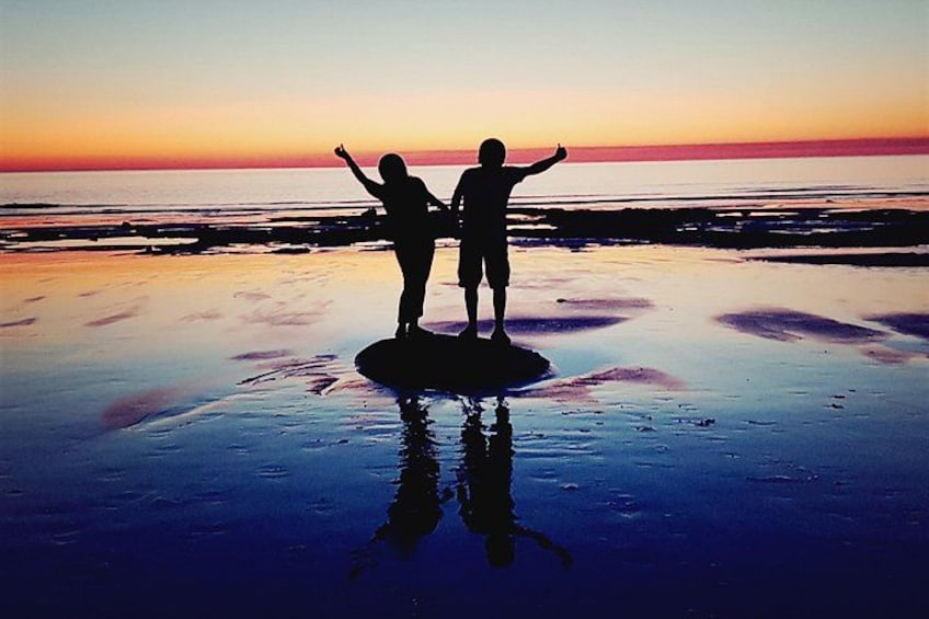 Two people standing on a wet beach at sunset. 3