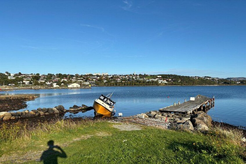 Ein Boot an einem Steg, eine Holzpromenade und eine Küstenlinie mit Häusern im Hintergrund. 2