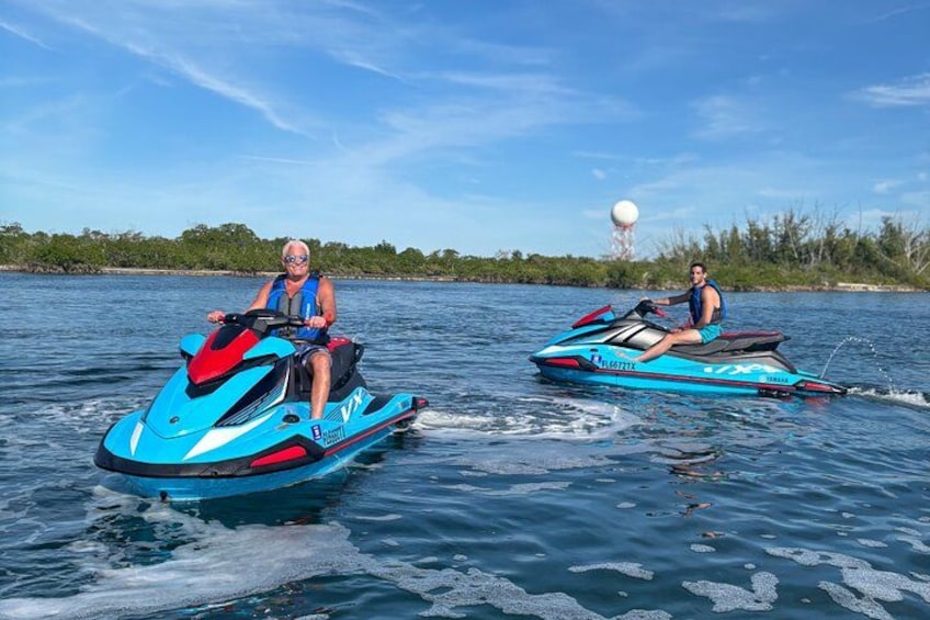 Two people jet skiing on a body of water with trees in the background. 2