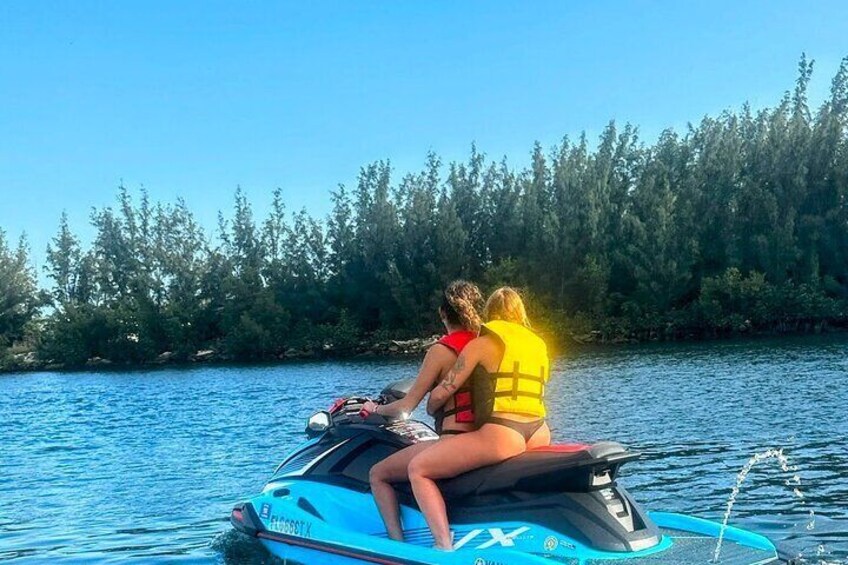 Dos personas en un jet ski, usando chalecos salvavidas, en un cuerpo de agua con árboles al fondo. 5