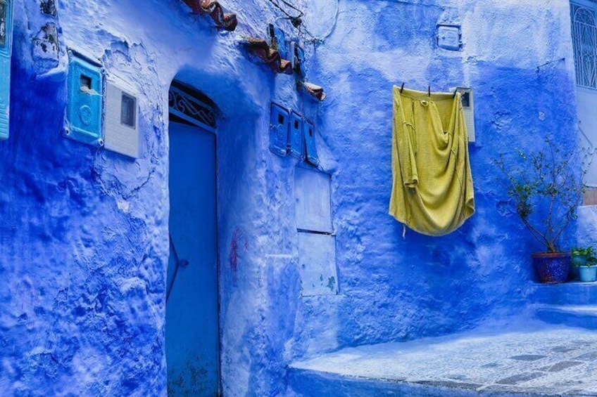 A blue-painted building with a door, a hanging yellow cloth, and potted plants. 5